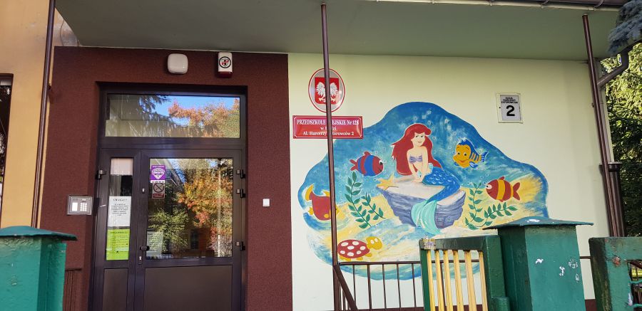 Wejście do Przedszkola Miejskiego nr 128 w Łodzi, na ścianie obok drzwi widoczny malunek z motywem dziecięcym syrenka Ariel.