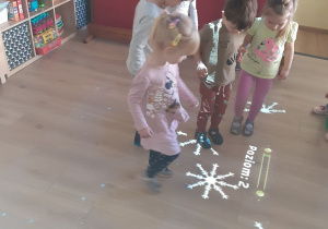 Dzieci z grupy żółtej nadeptują wyświetlane przez rzutnik na podłodze śniegowe gwiazdki, które pod wpływem ruchu wirują w kółko.