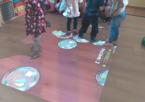 Dzieci z grupy żółtej nadeptują wyświetlane przez rzutnik na podłodze bańki, które pod wpływem ruchu pękają.