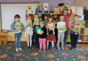 Na zdjęciu dzieci z grupy fioletowej stojące na dywanie w klasie prezentują kartki wielkanocne