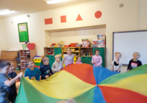 Na zdjęciu dzieci z grupy czerwonej świętują dzień przedszkolaka, dzieci bawią się chustą animacyjną na dywanie dzieci są roześmiane