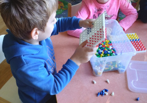 Na zdjęciu chłopiec i dziewczynka z grupy zielonej siedzą przy stoliku i układają małe klocki na białych tackach
