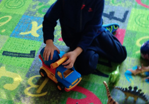 Na zdjęciu chłopczyk bawi się autkiem na dywanie