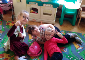 Na zdjęciu trzy dziewczynki bawią się w kąciku kuchennym dziewczynki pozują do zdjęcia leżąc dywanie w kąciku