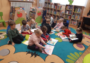 Dzieci siedzą na dywanie i oglądają wybrane przez siebie książki.