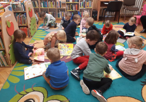 Dzieci oglądają książki siedząc na dywanie.