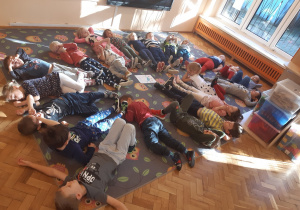 Dzieci leżą na dywanie słuchając muzyki relaksacyjnej.