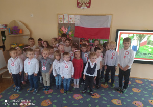 Dzieci z grupy żółtej i pomarańczowej w strojach galowych ustawione są w pozycji na baczność. Śpiewają hymn Polski "Mazurek Dąbrowskiego".