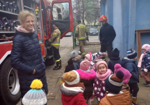 Dzieci stoją na podwórku, przy wozie strażackim.