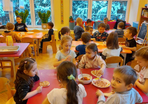 Na zdjęciu dzieci siedzą przy stołach i przygotowują pizze, dzieci się uśmiechają