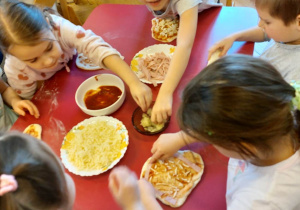 Na zdjęciu dzieci podczas przygotowania pizzy dzieci nakładają różne składniki na ciasto