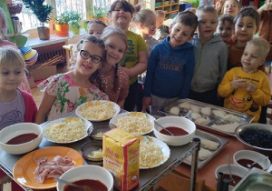 Na zdjęciu dzieci z grupy zielonej i fioletowej wokół dzieci produkty na pizze