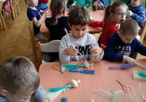 Na zdjęciu dzieci z grupy zielonej siedzą przy stole i wykonują anioły ze sznurka