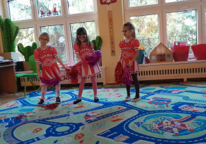 Na zdjęciu trzy dziewczynki z grupy zielonej w stroju Cheerleaderki, dziewczynki tańczą z pomponami