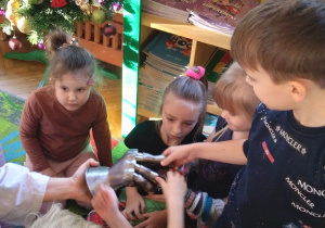 Na zdjęciu dzieci z grupy zielonej siedzą na dywanie i oglądają rękawice rycerza