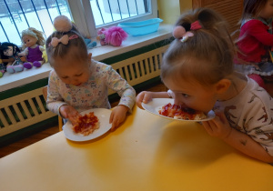 Dwie dziewczynki siedzą przy stole i konsumują swoją pizzę.