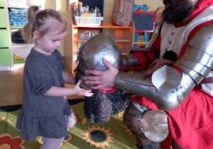 Przebrany za rycerza rodzic pokazuje dziewczynce hełm rycerski.