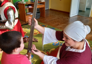 Przebrana za damę dworu mama pokazuje chłopcu miecz rycerski.