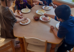 Dwie dziewczynki i dwóch chłopców przy stoliku przygotowują własnoręcznie pizzę.
