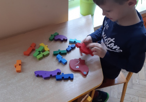 Chłopiec siedzi przy stoliku i układa puzzle "jamnika".