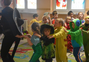 Na zdjęciu dzieci przebrane w stroje karnawałowe taczą w wężyka z nauczycielem