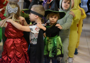 a zdjęciu dziewczynka przebrana za czarownice stoją ustawiona w wężyku z innymi dziećmi
