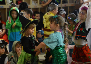Na zdjęciu dwie dziewczynki przebrane za czarownice i syrenkę Ariel tańczą razem ze sobą z tyłu pozostałe tańczące dzieci
