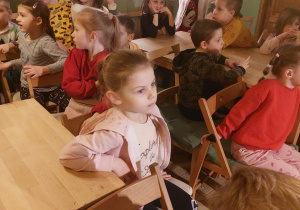 Na zdjęciu dzieci z grupy czerwonej siedzą na krzesełka i czekają na spektakl za dziećmi widać marionetki i kukiełki