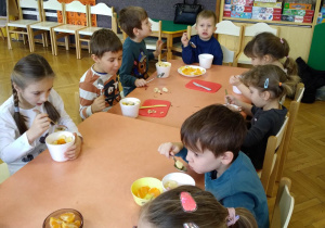 Na zdjęciu dzieci z grupy zielonej siedzą przy połączonych stołach dzieci jedzą wykonaną przez siebie sałatkę owcową