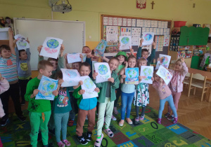 Na zdjęciu dzieci z grupy zielonej stoją w klasie, dzieci są ubrane na zielonej w rączkach trzymają kolorowanki z okazji Dnia Ziemi