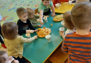 Dzieci siedzą przy stole. Robią sałatkę owocową- wkładają do kubeczków swoje ulubione owoce.
