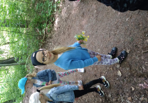 Na zdjęciu dziewczynka z grupy zielonej stoi w lesie w rączce trzyma kwiatki dziewczynka jest uśmiechnięta