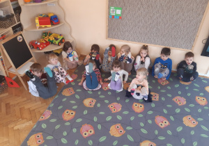 Dzieci siedzą na dywanie w sowy. Trzymają w górze nogi prezentując skarpetki nie do pary na znak tolerancji różnic między ludźmi.