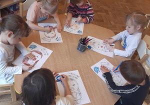 Pięć dziewczynek i jeden chłopiec siedzą przy stoliku. Kolorują "Skrzydlinki Motylinki"- obrazek przedstawiający dziewczynkę z zespołem Downa.