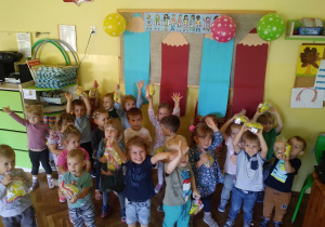 Na zdjęciu dzieci z grupy żółtej stoją nad tablicą i trzymają w ręku upominki z okazji dnia przedszkolaka