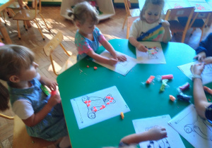 Na zdjęciu dzieci siedzące przy stoliku, dzieci wyklejają misie w kropki kawałkami plasteliny
