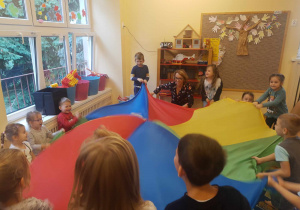 Dzieci zgrupy czerwonej siedzą na dywanie trzymają nad sobą kolorową chustę animacyjną