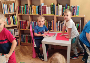 Na zdjęciu dzieci siedzące przy stoliku i oglądające książeczki w czytelni