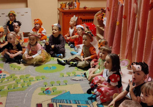 Na zdjęciach dzieci siedzą na dywanie na tle dekoracji jesiennej dzieci przebrane są w stroje o tematyce jesiennej