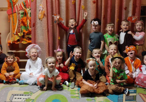 Na zdjęciu dzieci z grupy zielonej pozują na tle dekoracji jesiennej dzieci są przebrne w stroje o tematyce jesiennej