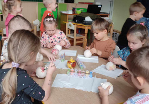 Na zdjęciu dzieci z grupy zielonej siedzą przy stoliku i malują ceramiczne bombki