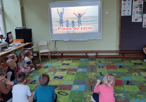 Dzieci z grupy zielonej siedzą na dywanie i oglądają film edukacyjny o prawach dziecka