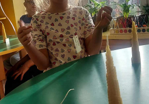 Na zdjęciu dziewczynka z grupy fioletowej podczas ozdabiania świeczki wstążeczką
