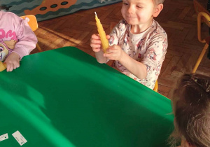 Na zdjęciu chłopiec siedzący z dziećmi przy stoliku, które wykonują świeczkę