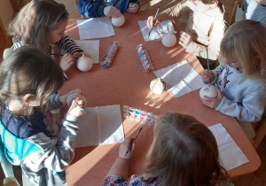 Przy stoliku siedzą cztery dziewczynki i dwóch chłopców. Malują farbami ceramiczne bombki.