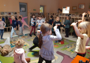 Dzieci na kolorowym dywanie tańczą w rytm muzyki w wybrany przez siebie sposób. W tle widać szafki na ubrania.
