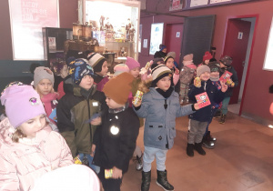 Dzieci ubrane w kurtki stoją na korytarzu. W rękach trzymają soki i ulotki repertuarowe kina. W tle widoczna jest zabytkowa kamera.
