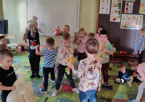 Na zdjęciu dzieci tańczące na dywanie, w rękach trzymają pluszowe misie i przytulanki