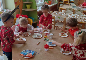 Na zdjęciu dzieci z grupy zielonej siedzą przy stołach i dekorują pierniczki, dzieci ubrane są w stroje koloru czerwonego o tematyce świątecznej