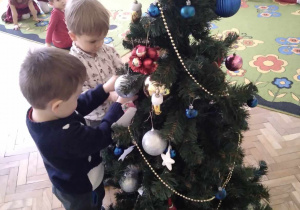 Na zdjęciu dwóch chłopców dekorujących choinkę.